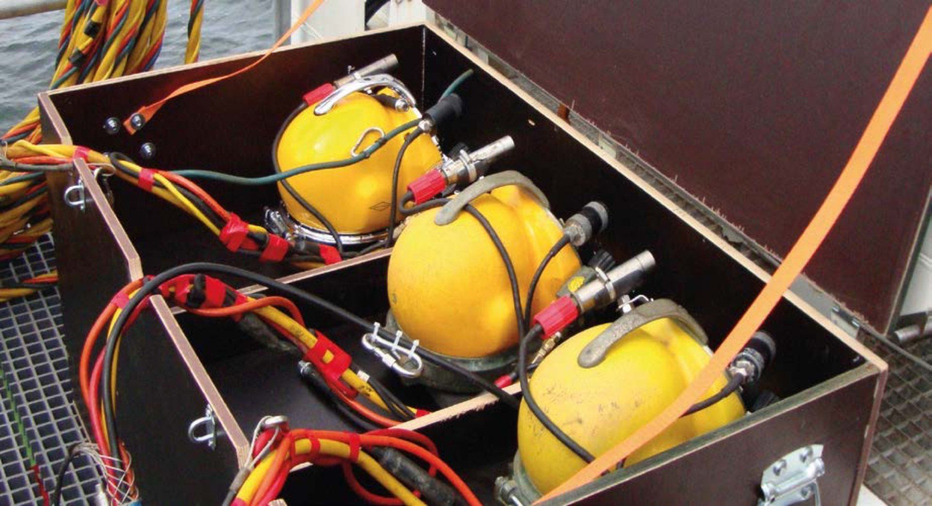Brown wooden box with three diving helmets , each with attached cables and metal components.
