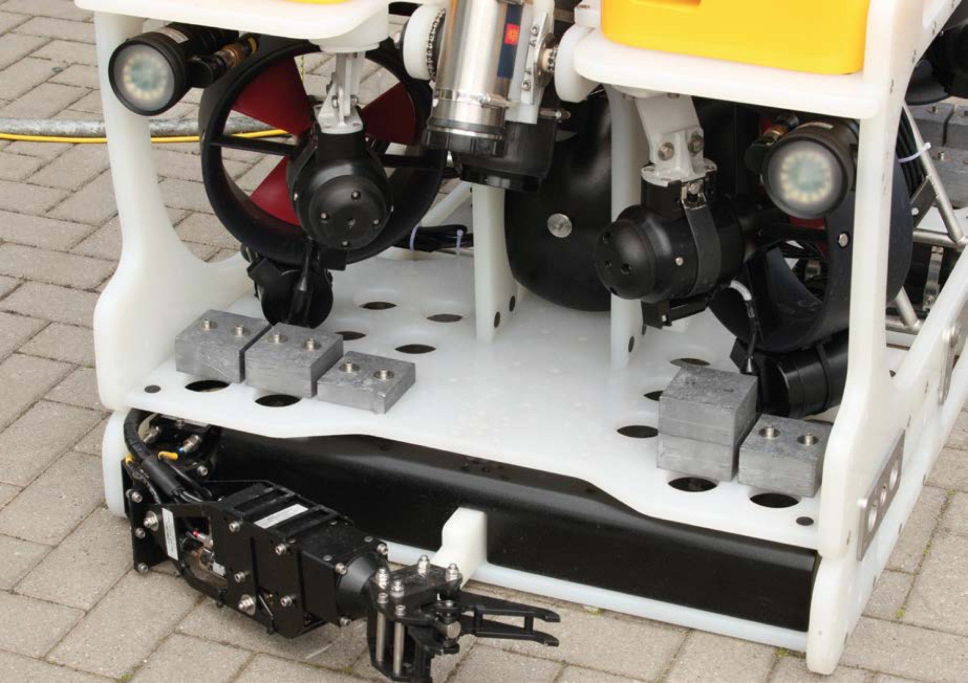 Close-up of a white and black underwater drone with propellers, lights, and a mechanical arm on a platform.