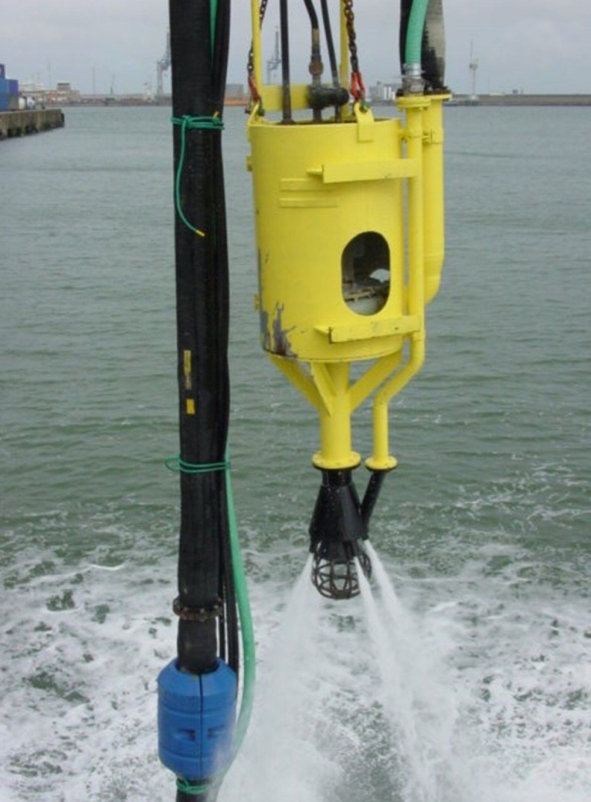 Yellow underwater pump spraying water. In a harbor.