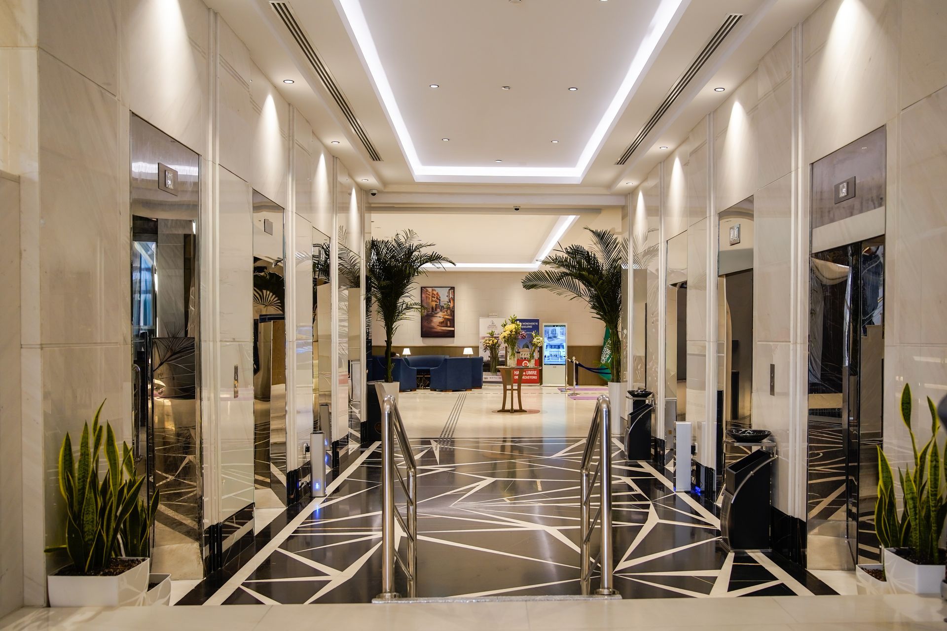 Luxury hotel lobby with marble floors, tall mirrors, and potted plants along a bright hallway.