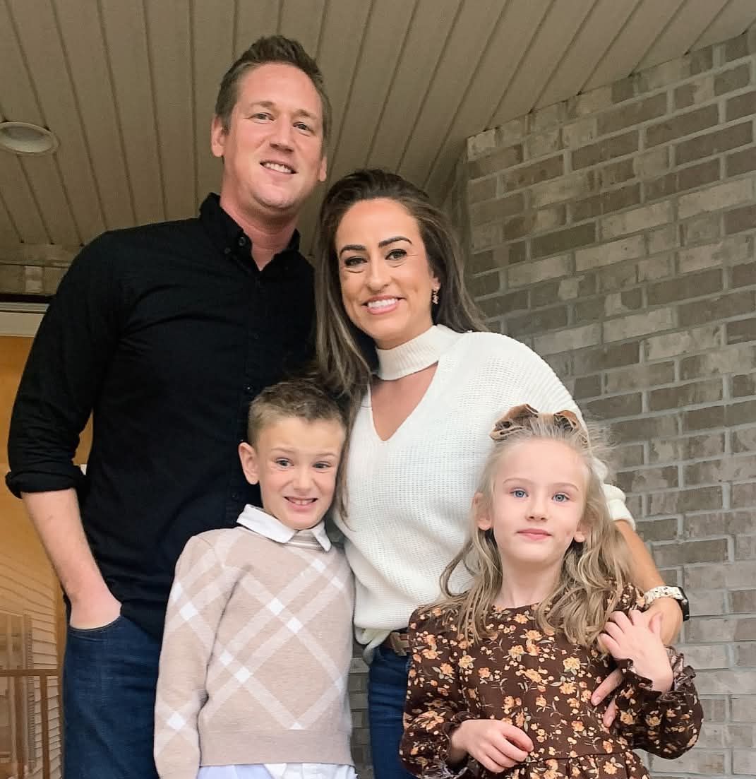 Family of four posing together; brick wall background.
