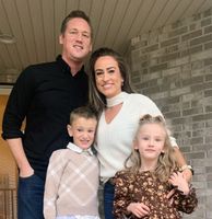 Family of four posing together; brick wall background.