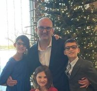 A man with three children pose near a decorated Christmas tree. They wear glasses and smile.