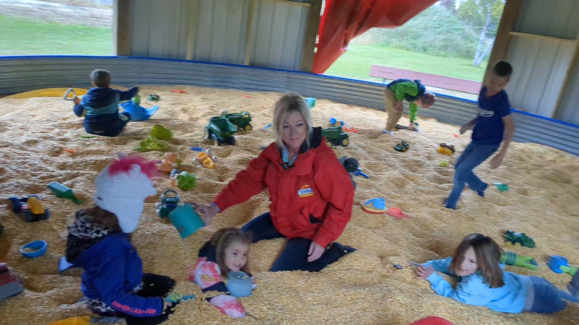 Children and an adult playing in a corn pit inside a barn.