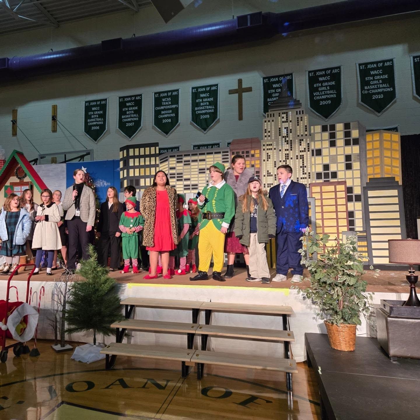 Students on stage during a play, in front of cityscape backdrop, wearing costumes.