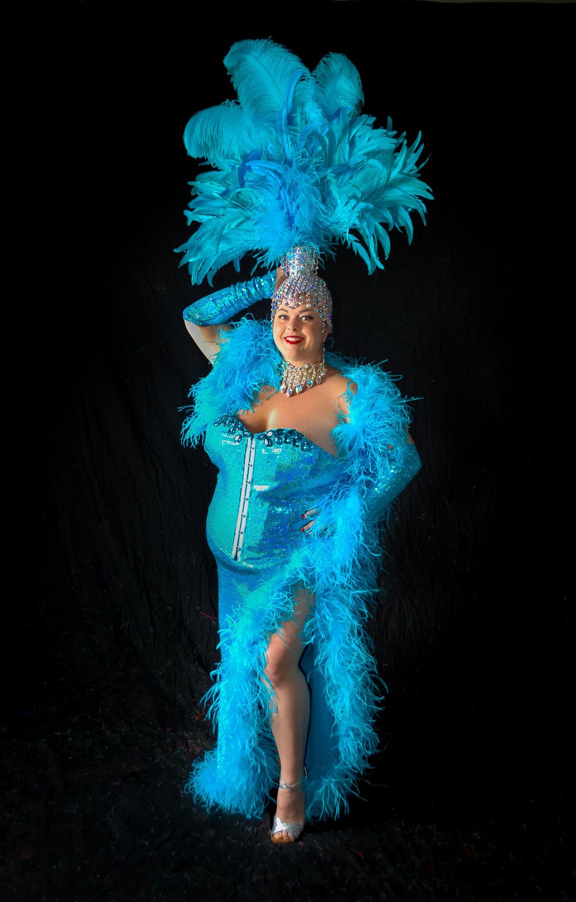 A woman in a blue feathered costume is standing in front of a black background.