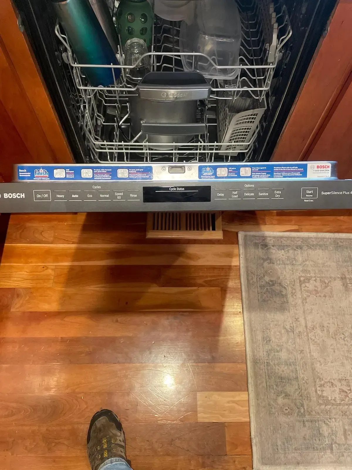 A person is standing next to a dishwasher with the door open.
