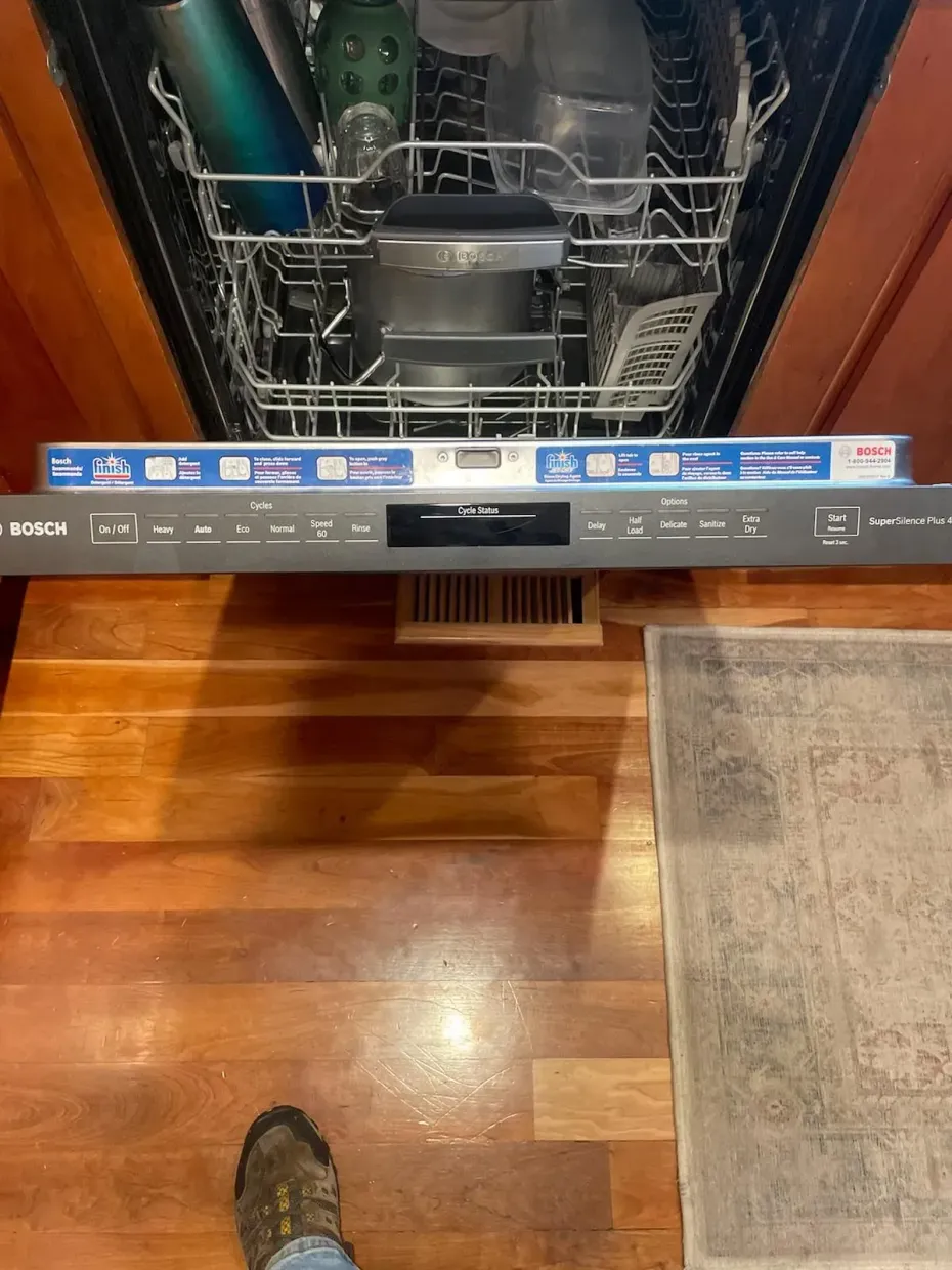 A person is standing next to a dishwasher with the door open.