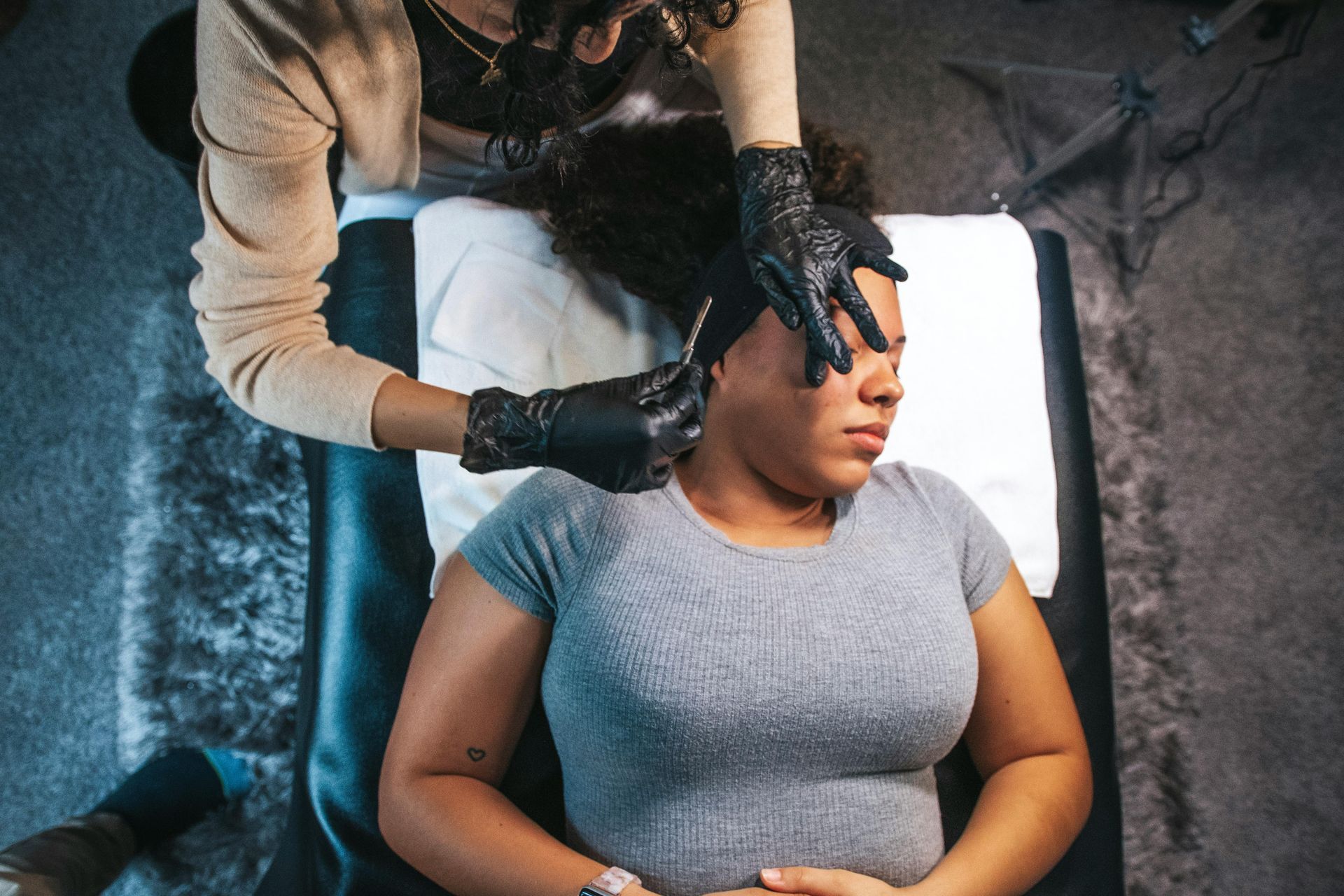Person getting an ear piercing by a gloved hand, indoors on a dark surface.