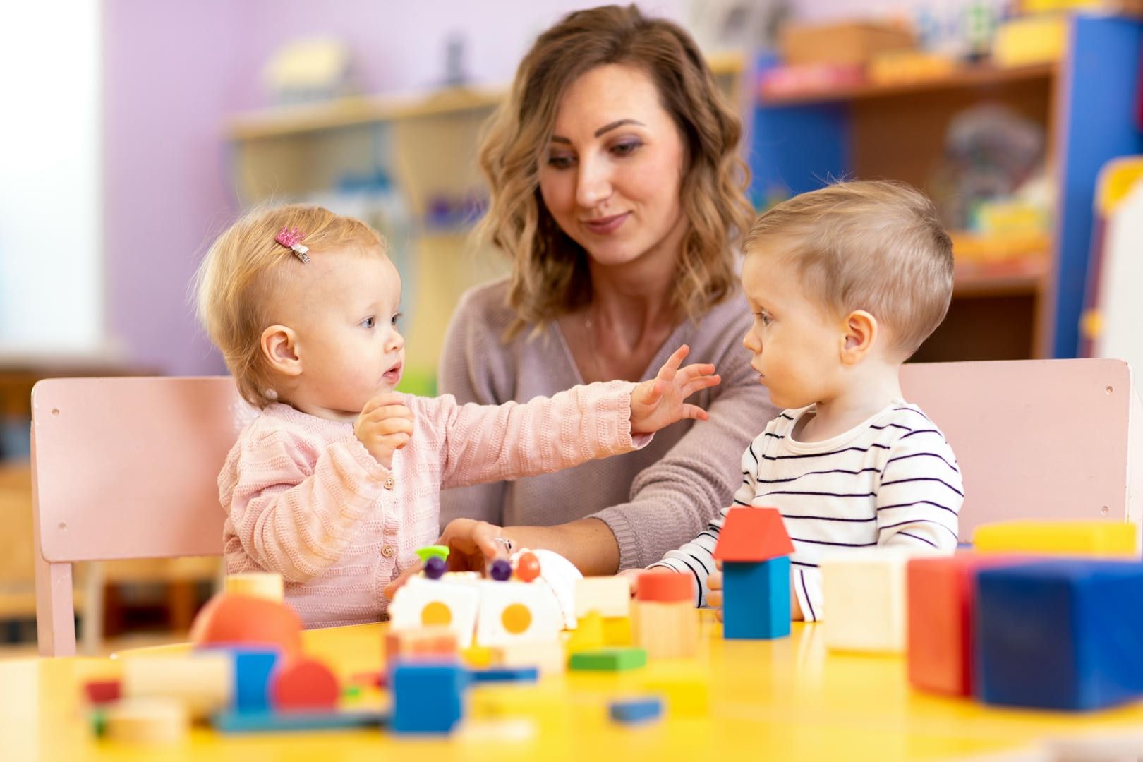 A woman is sitting at a table with two children playing with blocks.