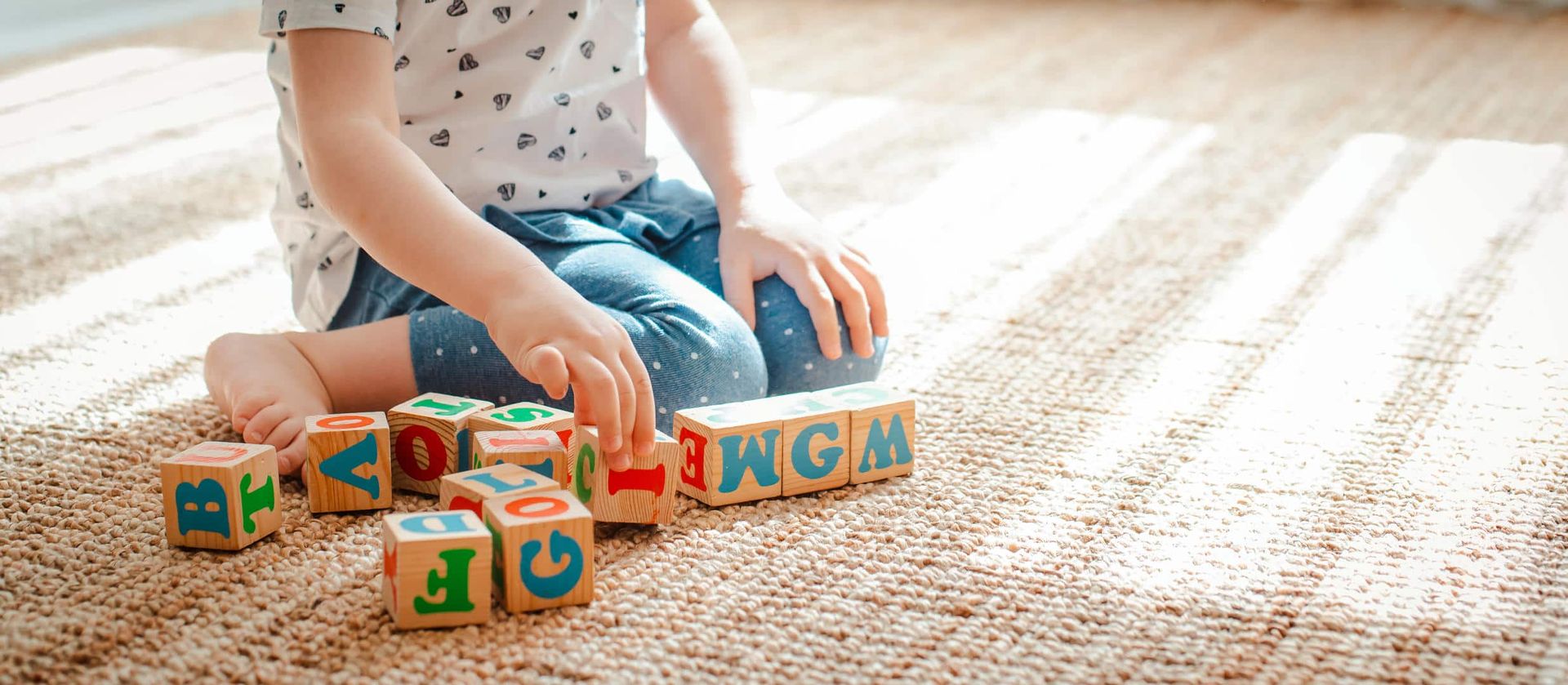 A little girl is sitting on the floor playing with wooden blocks.