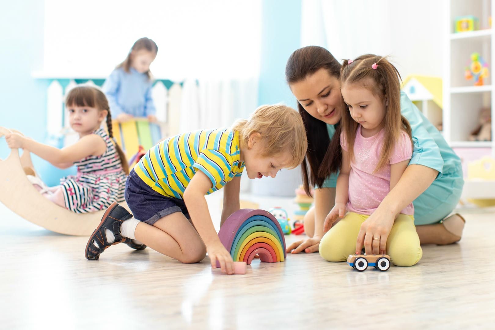 A woman and two children are playing with toys on the floor.