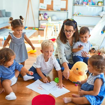A woman is sitting on the floor with a group of children.