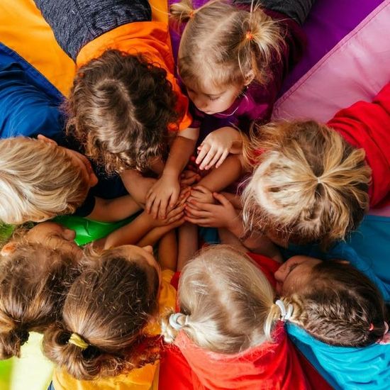 A group of children are laying in a circle with their hands together