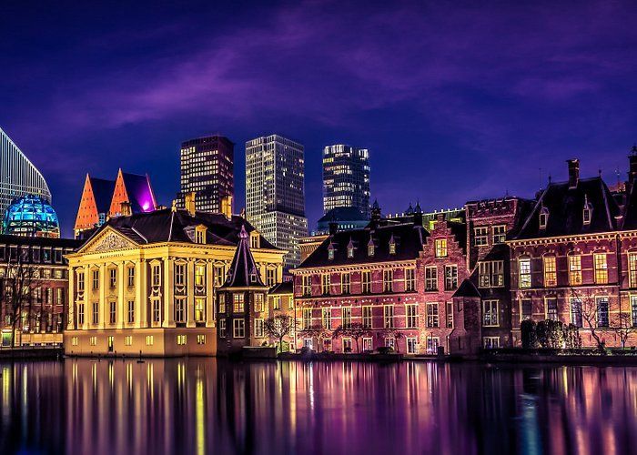 Een skyline van een stad bij nacht met verlichte gebouwen die weerspiegeld worden in het water.