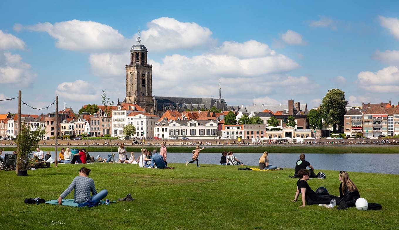 Een groep mensen zit op het gras bij een meer.