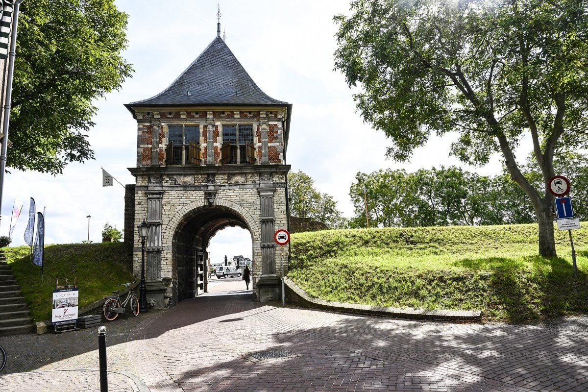 Een stenen boog met daarop een toren, omgeven door bomen.