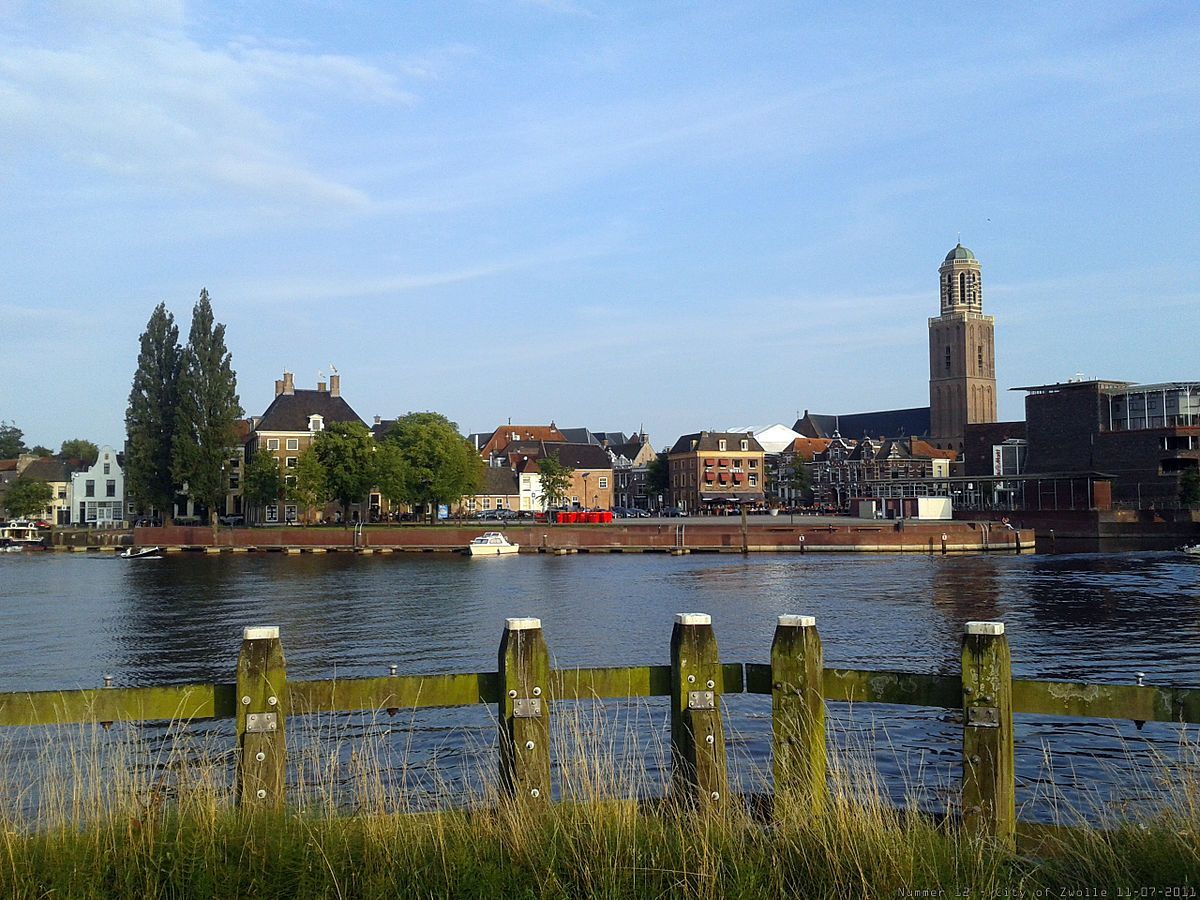 Een houten hek omringt een waterpartij met een stad op de achtergrond