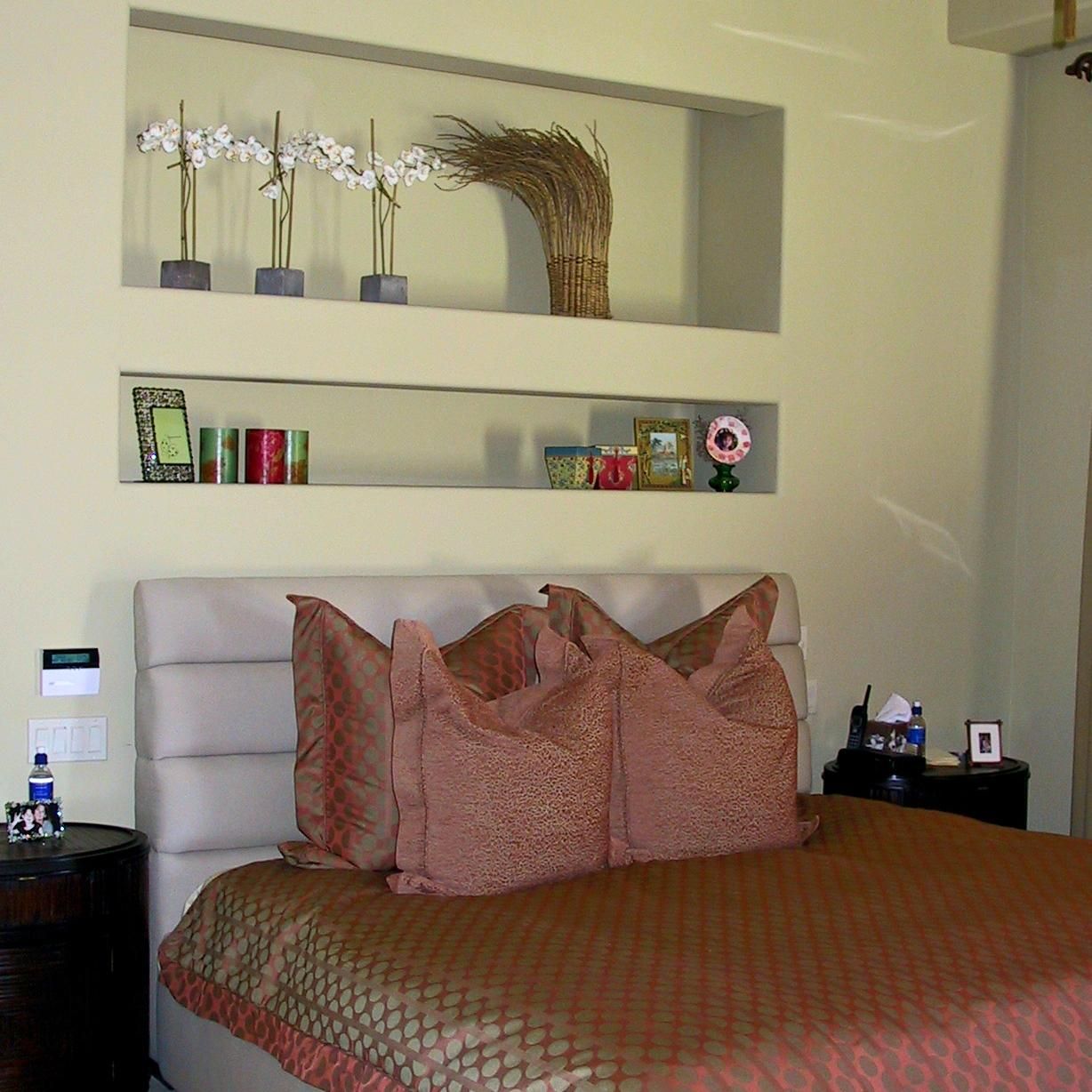 A bedroom with a bed and a shelf with flowers on it