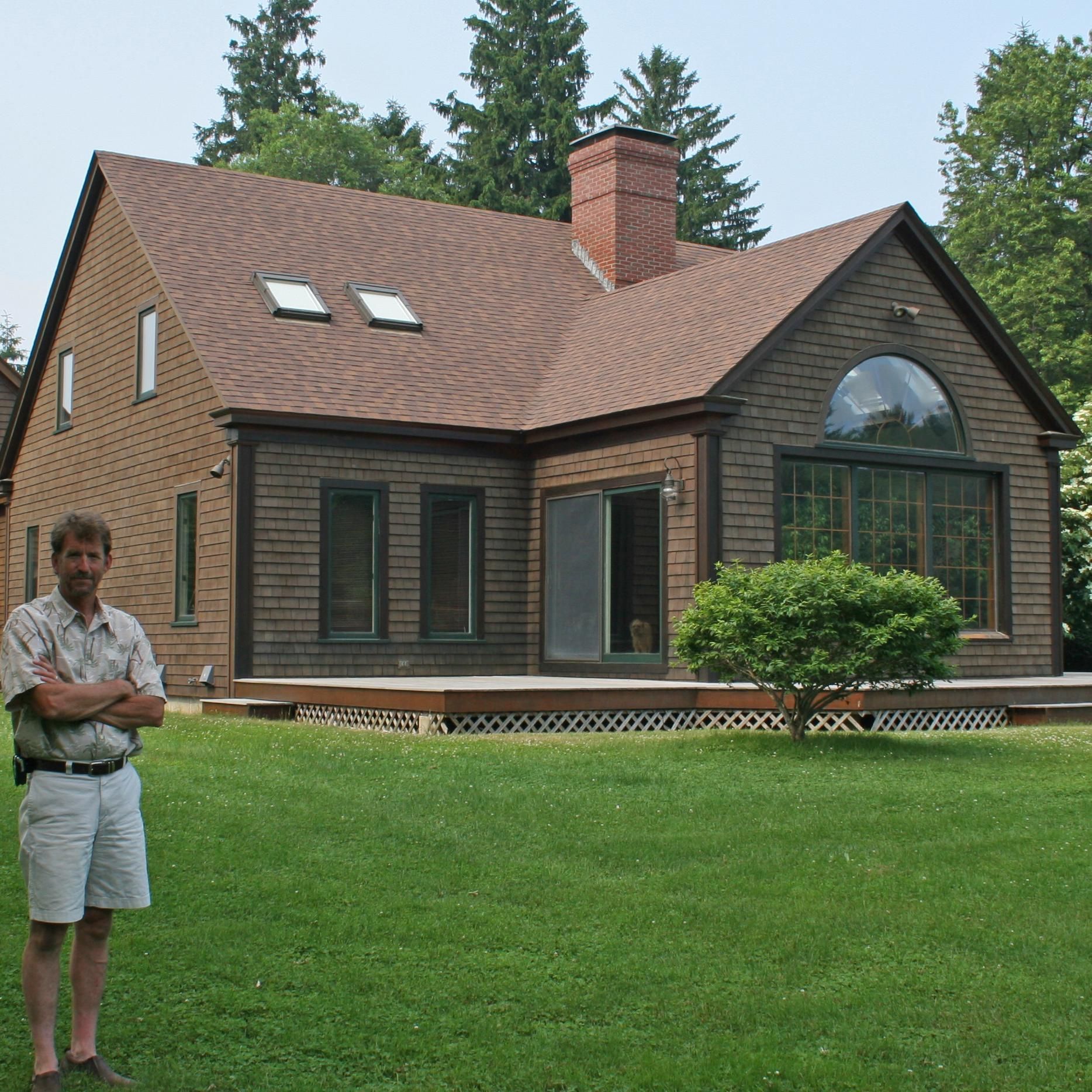 A man stands in front of a large house