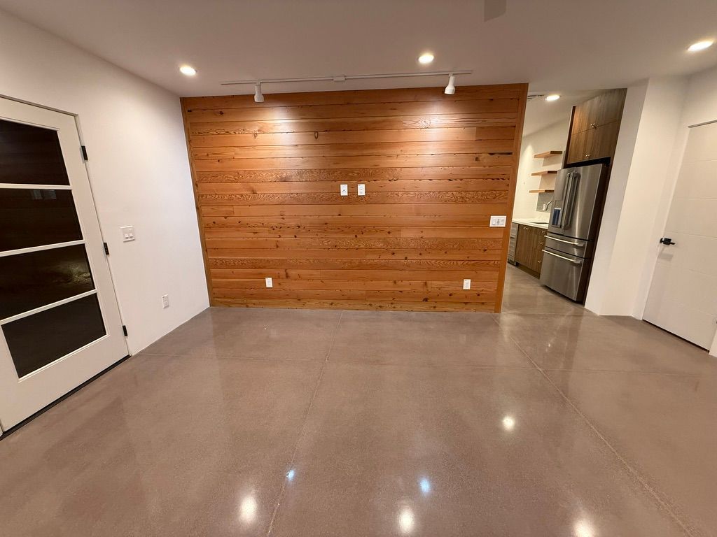 Empty modern room with polished floor, wood accent wall, recessed lights, and kitchen area to the right