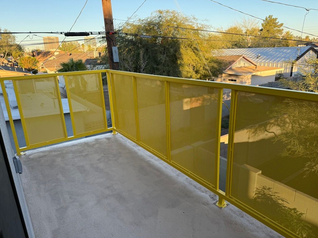 Yellow mesh balcony railing overlooking rooftops and trees in bright daylight