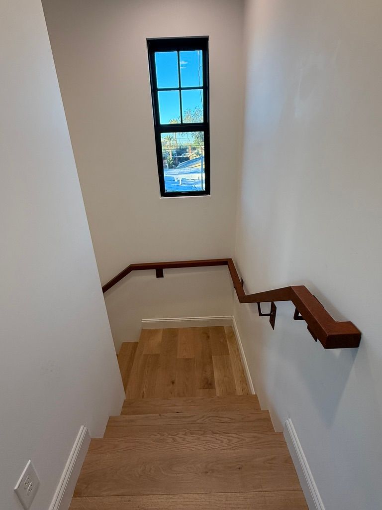 Stairwell with wooden stairs, white walls, dark handrail, and a small window at the landing.
