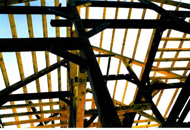 Wooden roof structure with beams and rafters against a bright sky.