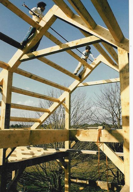 Two people work on wooden roof framing; clear sky in background.
