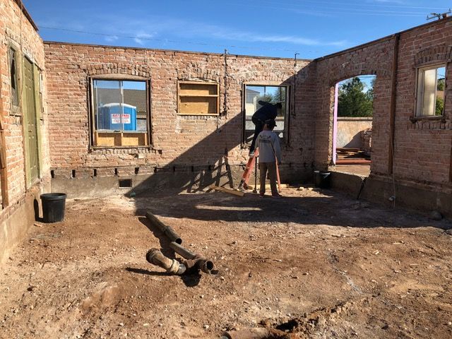 Construction site, exposed brick walls, two people standing, dirt floor.
