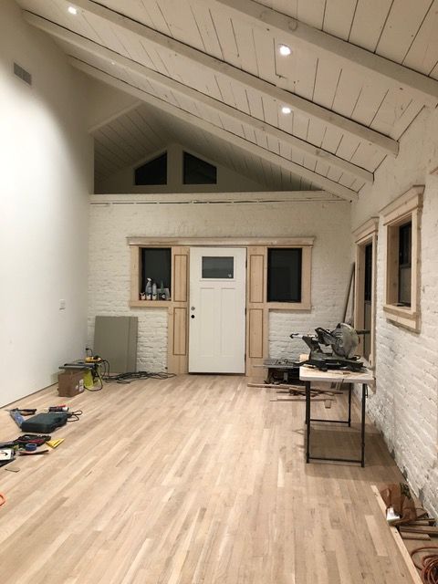 Interior view of a room under construction with white-painted brick walls, wood floor, and exposed beam ceiling.