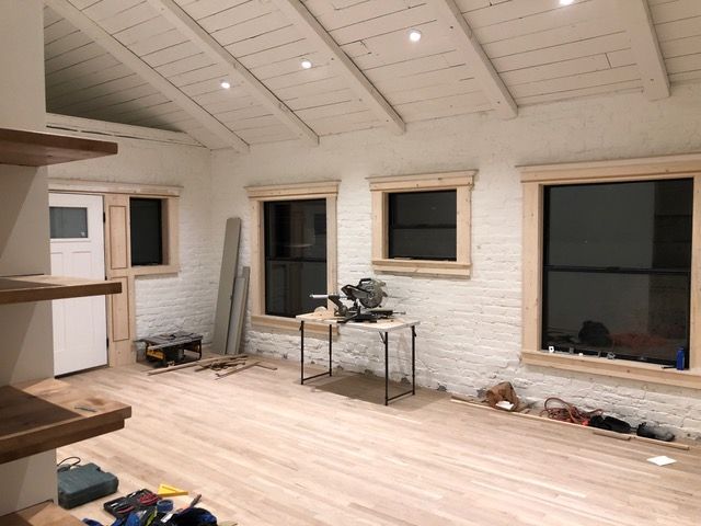 Interior construction: white brick walls, light wood floor, windows with wooden trim, and exposed beams on the ceiling.