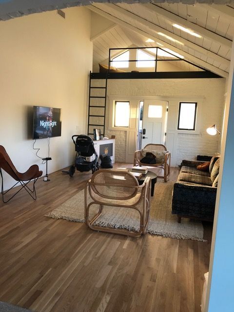 Cozy living room with wood floors, white walls, loft, small rug, couch, chairs, TV, and baby stroller.