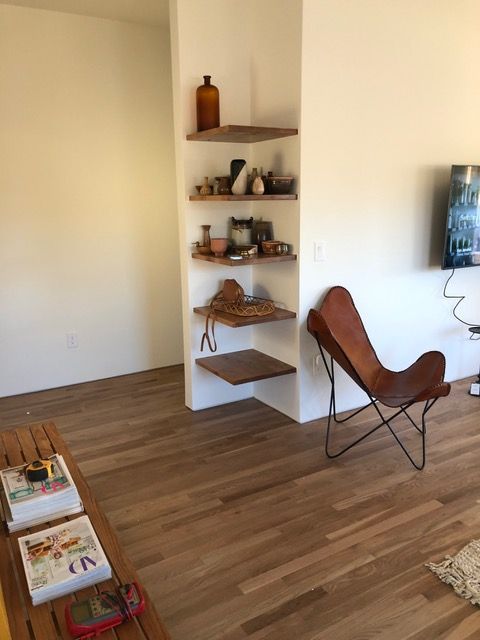 Built-in corner shelves with decor, wooden floors, brown leather butterfly chair, white walls.