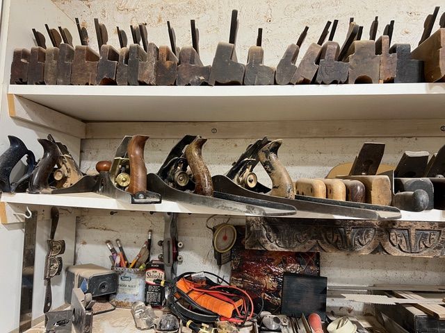Wooden hand planes and tools on a shelf in a workshop.