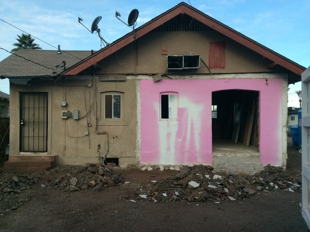 Back view of a house undergoing renovation, with a pink-painted section, rubble in foreground.