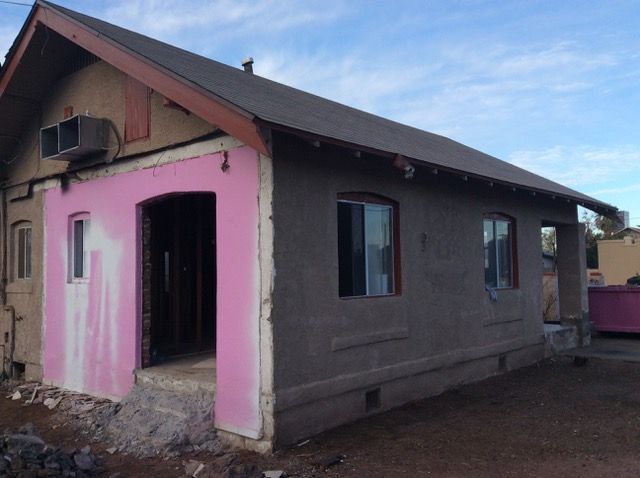 House under renovation, part pink, part gray stucco, with open doorway and windows.
