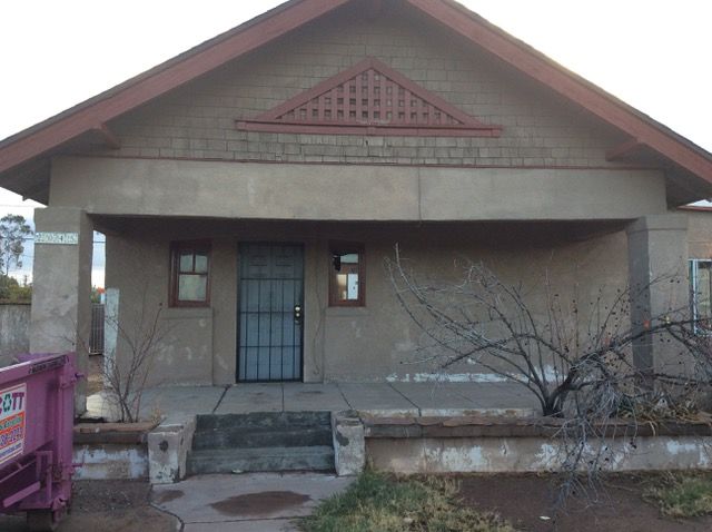 A stucco house with a porch, a gated front door, and a brown roof.