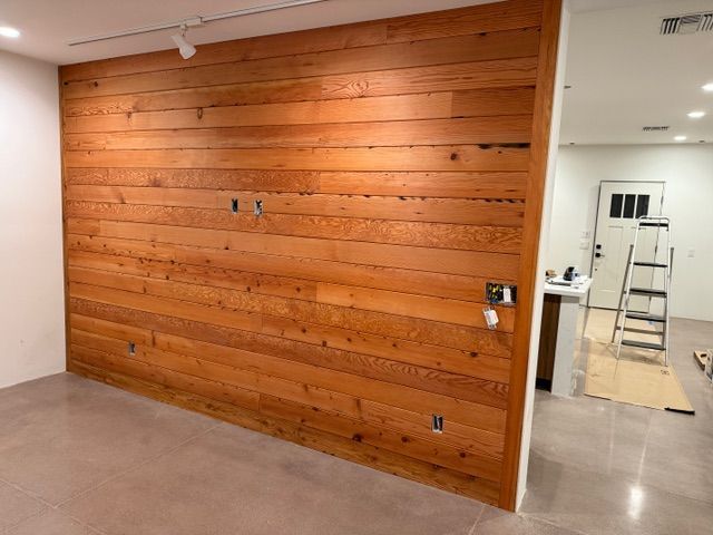 Wood-paneled wall in a room with white walls and a concrete floor. Electrical outlets are visible.