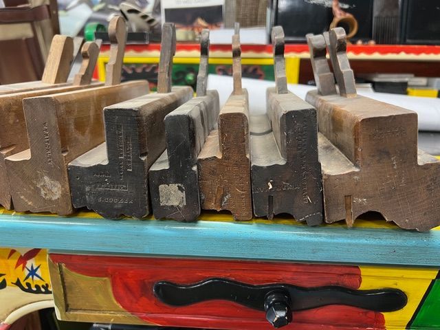 Close-up of a row of vintage wooden molding planes with varying shapes and wear, resting on a colorful table.