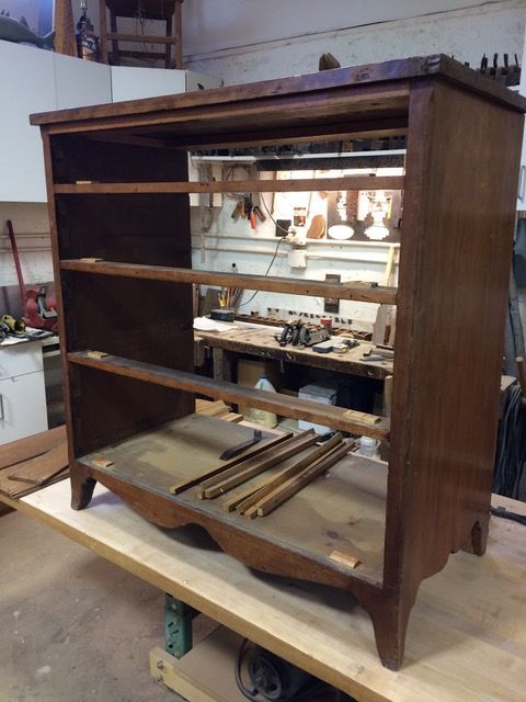 Wooden bookshelf frame, shelves missing, resting on a workbench in a workshop. Brown wood.