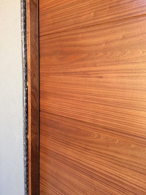Wooden door with visible wood grain, beside a light-colored wall and dark trim.