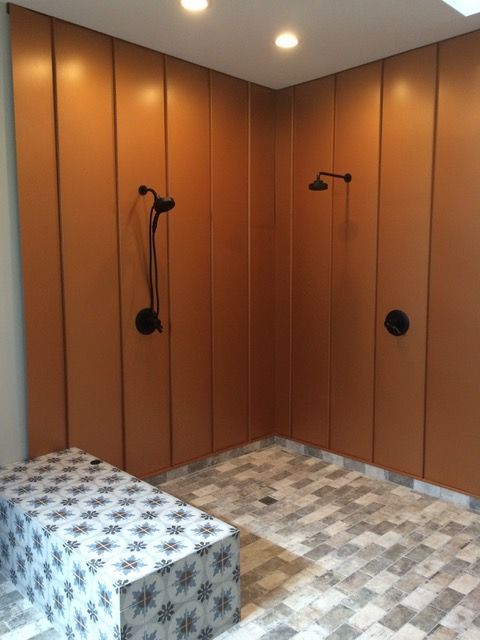 Shower with orange-brown wall panels, two shower heads, patterned floor, and a patterned bench.