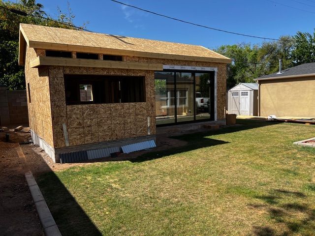 Backyard construction: Unfinished wooden structure with large glass doors. Green grass and blue sky.