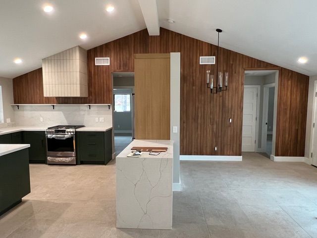 Modern kitchen with dark green cabinets, wood panel walls, and a white island.