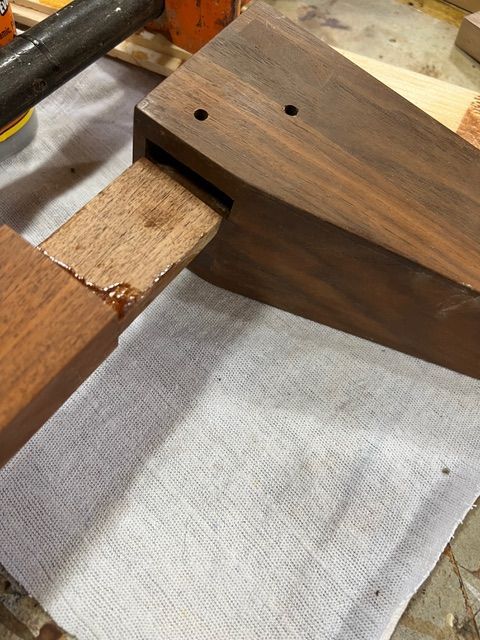 Wooden pieces being glued together; clamp in background.