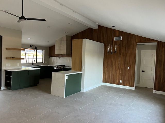 Modern kitchen with green cabinets, wood accents, and gray tile flooring.