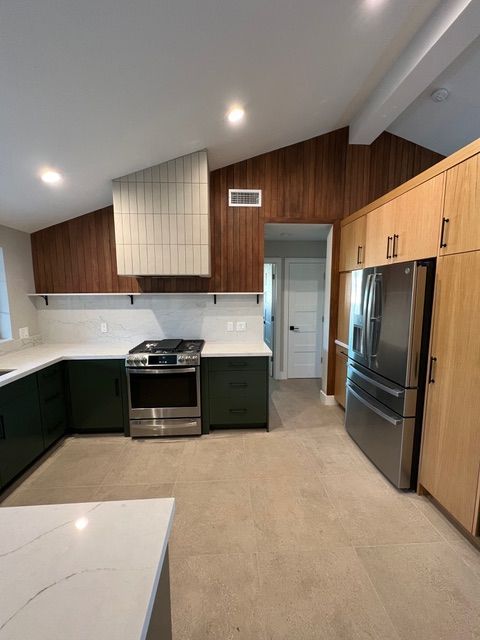 Modern kitchen with dark green cabinets, white countertops, stainless steel appliances, and wood paneling on the walls.