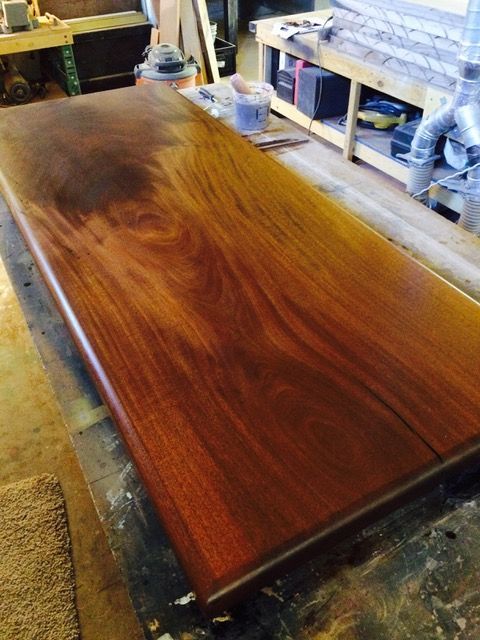 Finished wooden tabletop with a glossy, reddish-brown finish, sitting on a work table in a workshop.