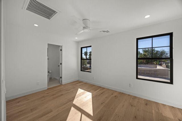 Empty white-walled room with hardwood floors, two windows with black frames, and a ceiling fan.